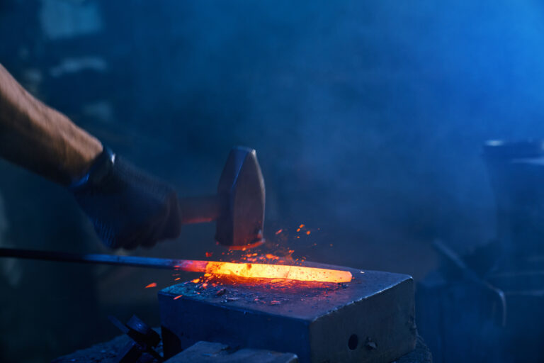 close up strong male hands forging molten metal anvil